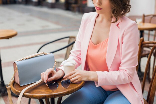Feche detalhes de acessórios de mulher elegante sentada em um café bebendo café, óculos escuros, bolsa, tendência da moda primavera verão, estilo elegante