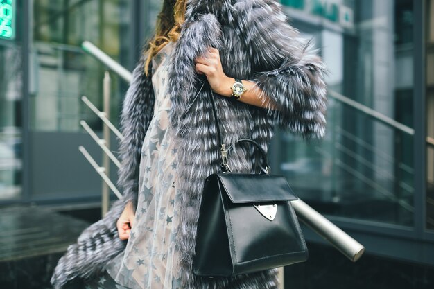 Feche detalhes de acessórios de uma mulher elegante andando pela cidade com um casaco de pele quente, inverno, clima frio, segurando uma bolsa de couro, tendência da moda de rua
