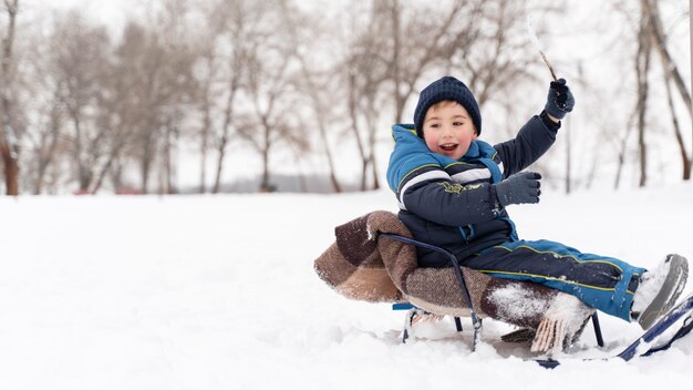 Feche e uma criança feliz brincando na neve