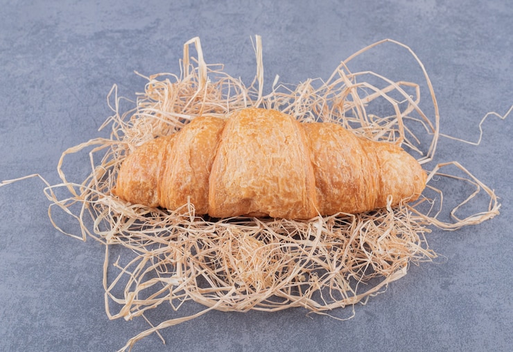 Foto grátis feche foto de croissant francês fresco na palha sobre fundo cinza.