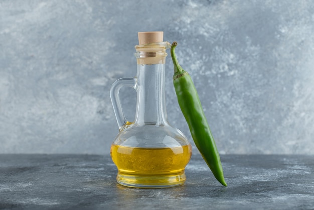 Feche foto de pimenta verde com garrafa de óleo em fundo cinza