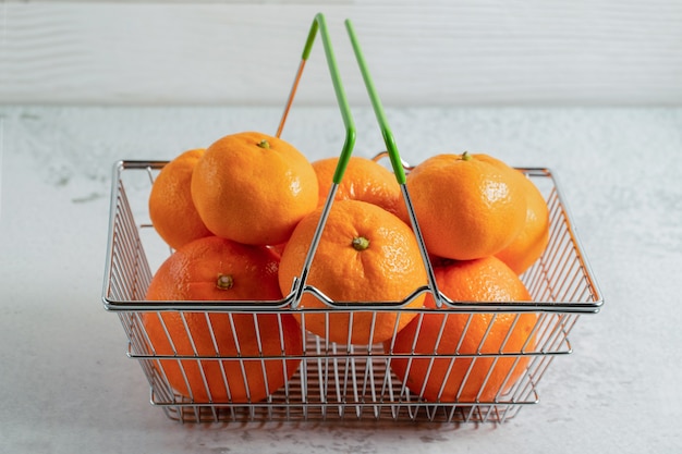 Feche foto de tangerinas frescas de clementina na cesta na superfície cinza.