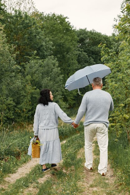 Feche o casal romântico caminhando em um parque de outono. Homem e mulher vestindo blusas azuis. Homem segurando um guarda-chuva.