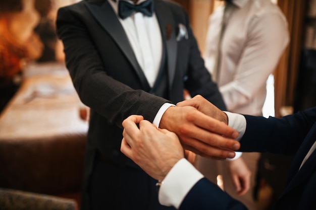 Feche o homem ajudando o noivo a se vestir e ajustando as mangas do terno antes da cerimônia de casamento