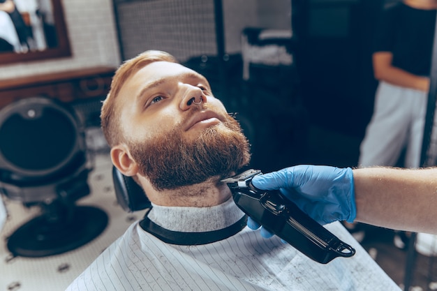 Feche o homem cortando o cabelo na barbearia usando máscara durante a pandemia de coronavírus.