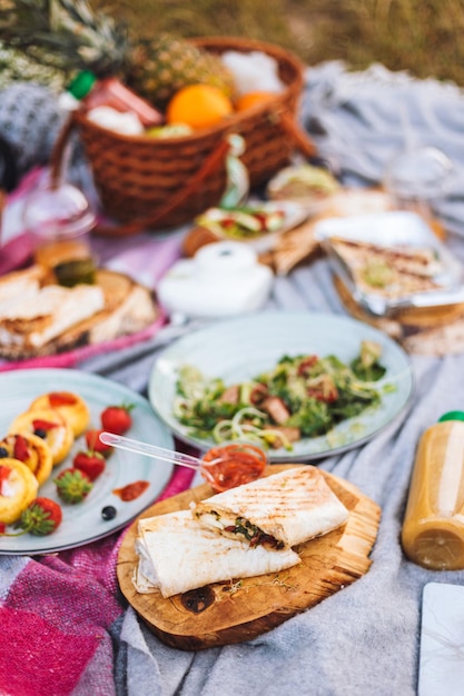 Foto grátis feche o piquenique moderno com variedade de comidas e bebidas saborosas na manta de piquenique no parque