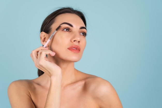 Feche o retrato da beleza de uma mulher com pele perfeita e maquiagem natural, lábios carnudos e nus, segurando uma escova de sobrancelha