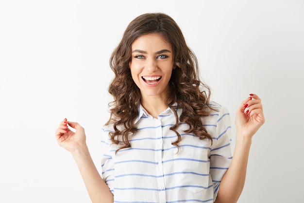 Feche o retrato da expressão do rosto sorridente de uma jovem bonita, segurando as mãos, sucesso, vencedor, vestida com camisa isolada, feliz, humor positivo, sorriso sincero, cabelo longo cacheado, dentes brancos