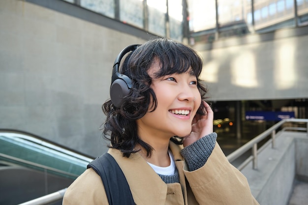 Feche o retrato da menina coreana em fones de ouvido estudante ouve música em fones de ouvido e sorri anda