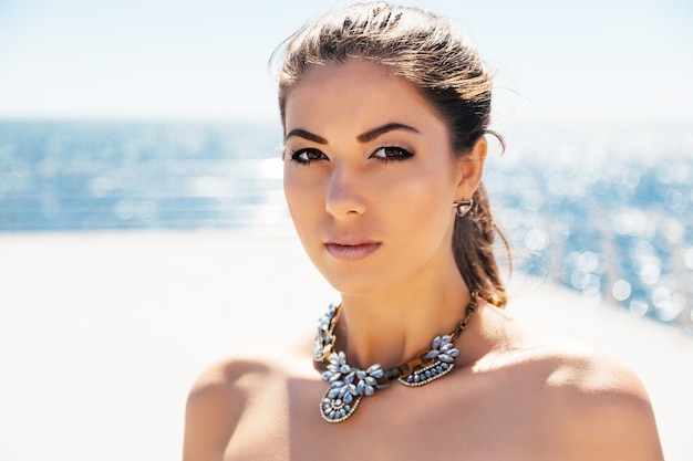 Feche o retrato da moda da jovem mulher bonita elegante colar de diamantes grande posando à beira-mar. Cores claras e limpas.