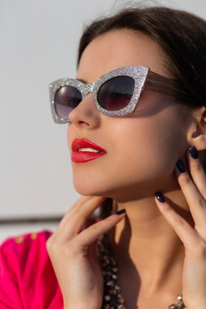 Feche o retrato da mulher morena elegante em elegantes óculos de sol e camiseta rosa.