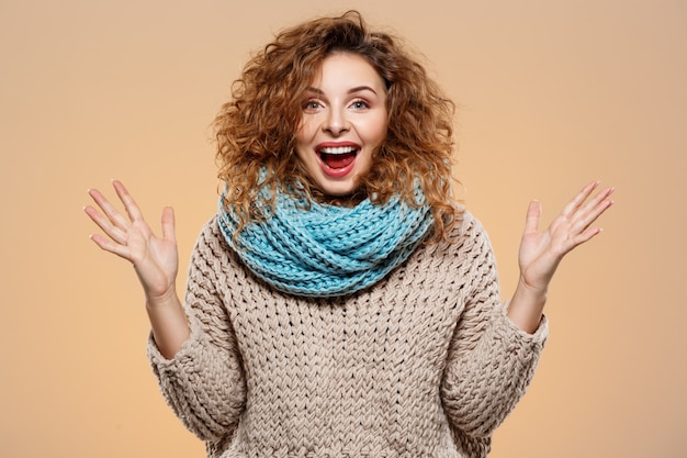 Feche o retrato de alegre surpresa sorridente menina morena morena bonita camisola de malha e pescoço cinza sobre parede bege