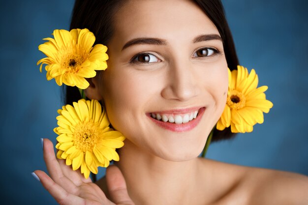 Feche o retrato de concurso jovem com flores amarelas sobre parede azul