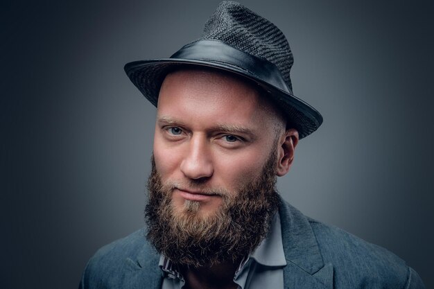 Feche o retrato de estúdio de macho barbudo em um chapéu de feltro em fundo cinza.