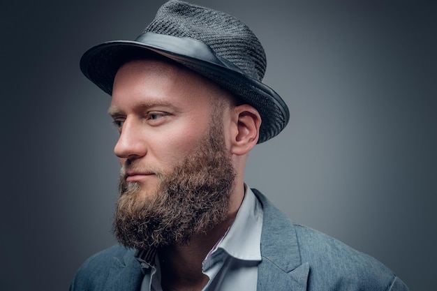 Feche o retrato de estúdio de macho barbudo em um chapéu de feltro em fundo cinza.
