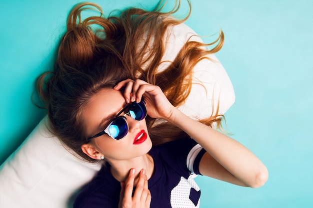 Feche o retrato de estúdio de moda elegante mulher bonita com óculos de sol elegantes. Lábios vermelhos fundo azul.