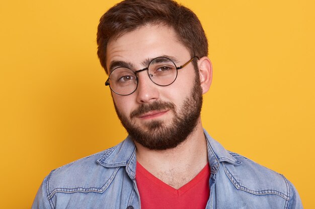 Feche o retrato de jovem bonito carismático, com barba, olhando diretamente, tendo feliz expressão facial