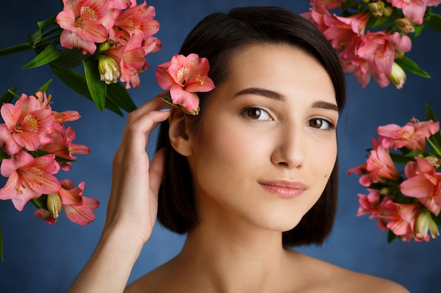 Feche o retrato de jovem concurso com flores sobre parede azul