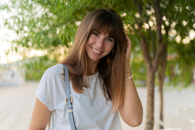 Feche o retrato de rir feminino europeu em t-shirt branca, posando no parque.