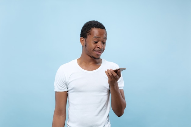 Feche o retrato de um jovem afro-americano de camisa branca ... falando no smartphone ou gravando uma mensagem de voz.