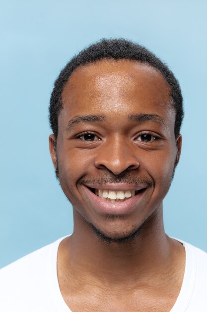 Feche o retrato de um jovem afro-americano em uma camisa branca na parede azul. Emoções humanas, expressão facial, anúncio, conceito de vendas. Parece feliz sorrindo, eu