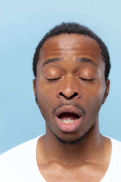 Feche o retrato de um jovem afro-americano em uma camisa branca sobre fundo azul. Emoções humanas, expressão facial, anúncio, conceito de vendas. Alguns segundos antes do espirro.