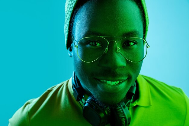 Foto grátis feche o retrato de um jovem afro-americano feliz sorrindo contra o estúdio de néon preto