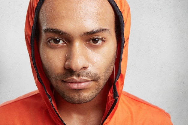 Foto grátis feche o retrato de um jovem atraente usando capuz, com a pele molhada depois de correr em tempo chuvoso