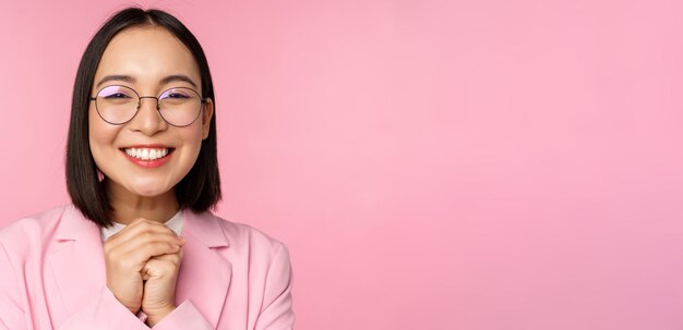 Feche o retrato de uma empresária feliz sorridente em óculos apertando as mãos agradecidas animadas por smth implorando ou diga por favor em pé sobre fundo rosa
