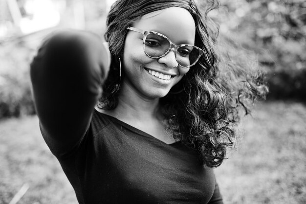 Feche o retrato de uma garota afro-americana em óculos de sol roupas pretas posadas ao ar livre Mulher negra na moda