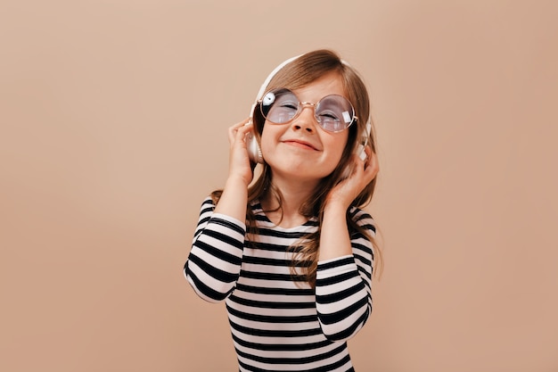 Feche o retrato de uma garota linda e charmosa vestindo uma camiseta despojada, ouvindo música com um sorriso feliz e os olhos fechados