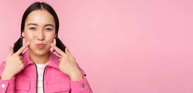 Foto grátis feche o retrato de uma jovem asiática mostrando suas covinhas cutucando bochechas bobas e fazendo caretas