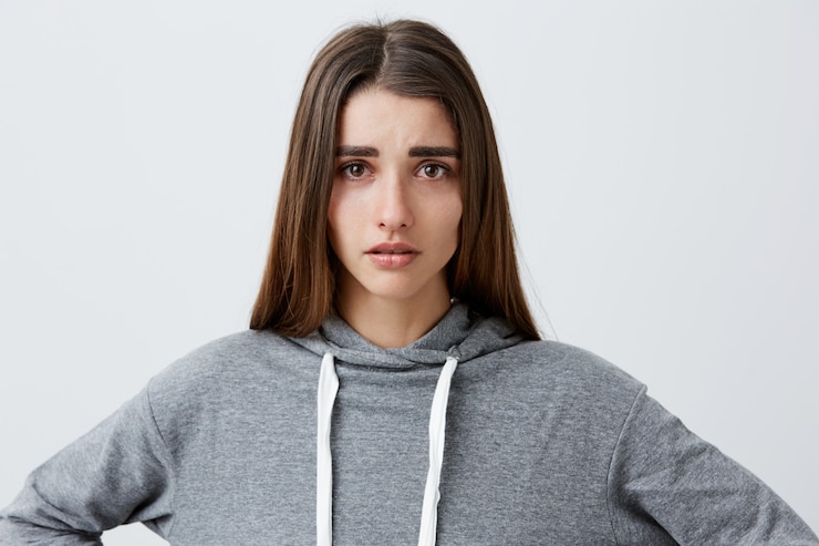 Foto grátis feche o retrato de uma jovem garota bonita e infeliz caucasiana com cabelos longos escuros no capuz cinza casual chorando, com os olhos molhados após a separação com o namorado. emoções negativas