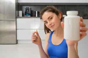 Foto grátis feche o retrato de uma jovem instrutora de fitness mostrando uma garrafa de vitaminas tomando brotos