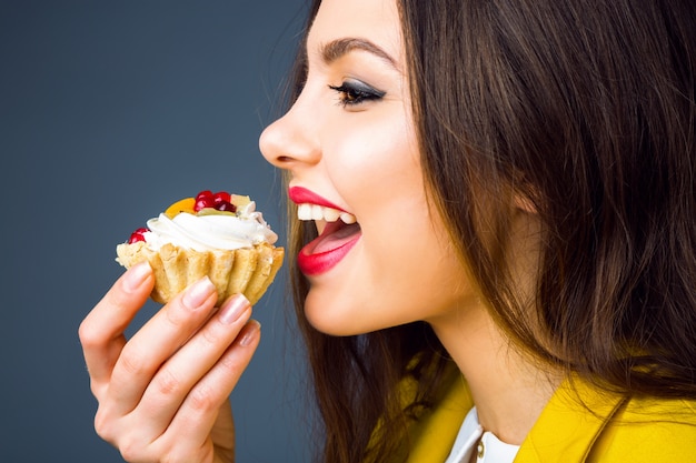 Foto grátis feche o retrato de uma jovem morena com maquiagem brilhante, comendo bolo saboroso com frutas e creme.