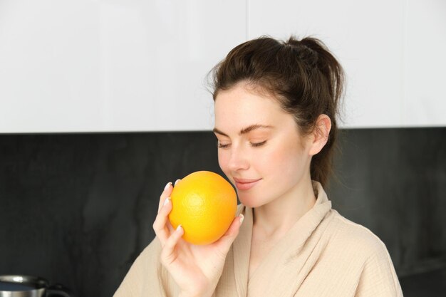 Feche o retrato de uma jovem morena que cheira suco de laranja fresco em vidro desfrutando de saúde