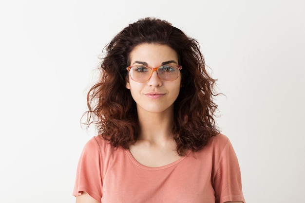 Feche o retrato de uma jovem mulher bonita hippie natural com penteado encaracolado em uma camisa rosa posando usando óculos isolados no fundo branco do estúdio