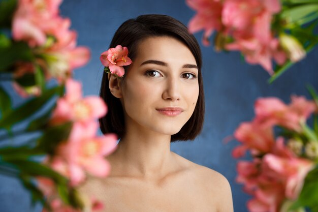Feche o retrato de uma jovem mulher concurso com blured flores cor de rosa sobre parede azul