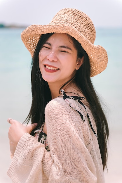 Feche o retrato de uma linda mulher asiática usando chapéu de emoção feliz na praia no verão de férias
