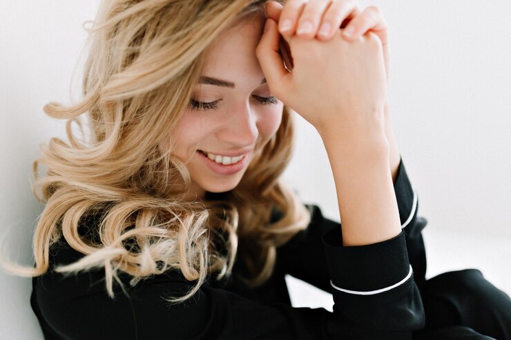 Foto grátis feche o retrato de uma mulher bonita e charmosa com cabelos loiros ondulados sorrindo com os olhos fechados