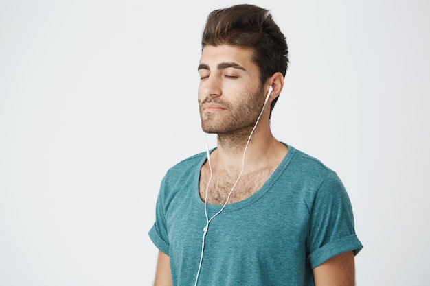 Feche o retrato do homem caucasiano maduro relaxado, vestindo camisa azul, com expressões de rosto calmo e olhos fechados, ouvindo música durante ioga de manhã.
