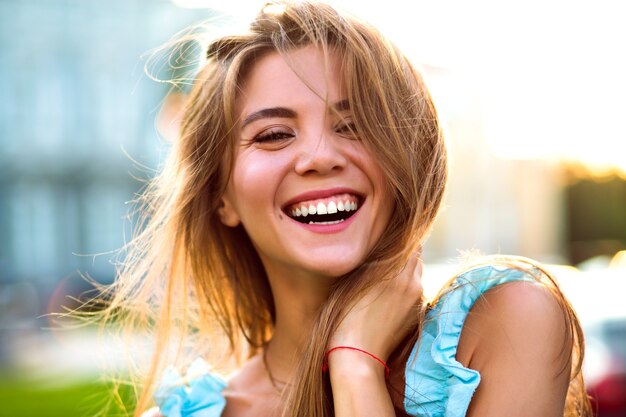 Feche o retrato ensolarado de uma linda mulher magnífica com maquiagem natural e grande sorriso incrível, olhando para a câmera, luz solar intensa, humor positivo.