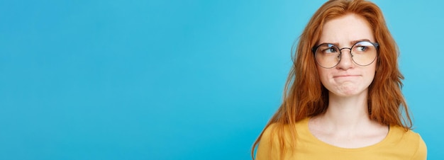 Foto grátis feche o retrato jovem linda e atraente ruiva com preocupação de óculos com algo azul pa