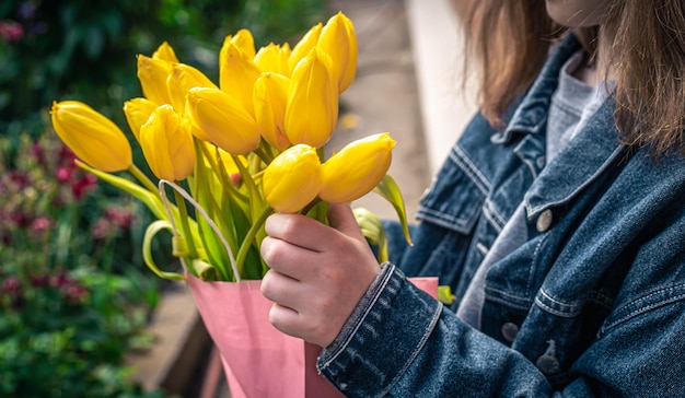 Feche um buquê de tulipas amarelas nas mãos de uma garotinha