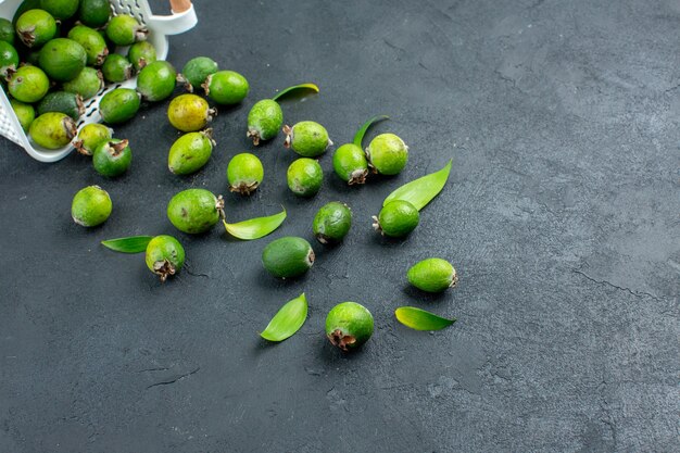 Feijoas frescas espalhadas por baixo de uma cesta de plástico em uma superfície escura com espaço de cópia