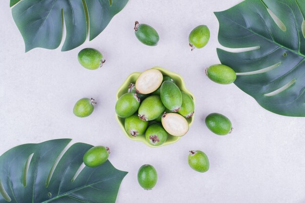 Feijoas verdes em uma xícara verde com folhas ao redor