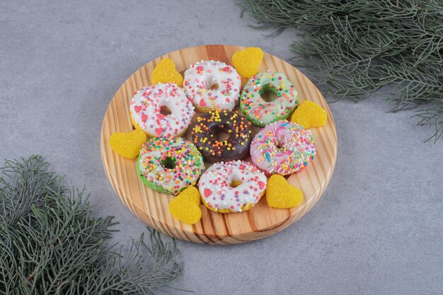 Feixes de galhos de pinheiro ao lado de donuts e marmeladas em uma bandeja na superfície de mármore