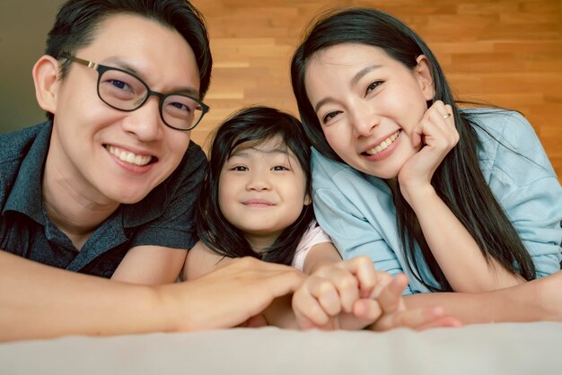 Felicidade alegre família asiática mãe pai filha deitada junto com diversão jogar beijo na cama retrato de família asiática fundo doméstico