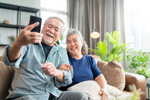 Felicidade velho casal de aposentados asiáticos desfruta de videochamada para a família juntos no sofá na sala de estar em homeasiáticos usam comunicação por smartphone para o conceito de ides de isolamento doméstico familiar