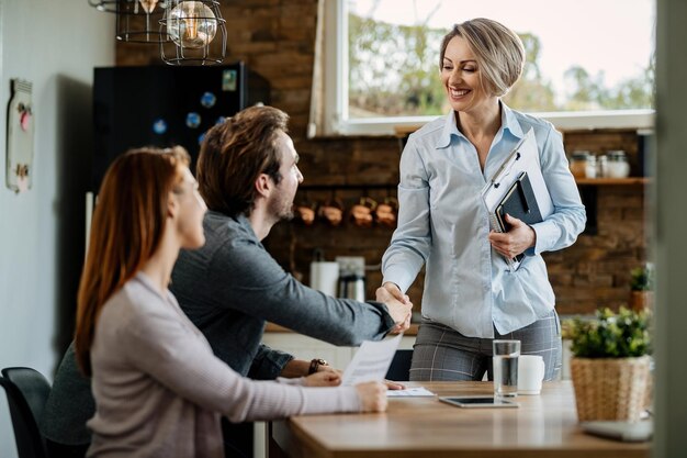 Feliz agente de seguros se encontrando com um jovem casal e apertando as mãos de um homem em sua casa